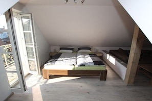 A bedroom with a sloped ceiling, a bed with a wooden frame, and a window with a view of buildings outside. - Holiday apartment with 2 bedrooms (Bamberg)