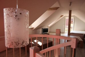 A room with a sloped ceiling, a television, and a staircase with a railing. - Holiday apartment with 2 bedrooms (Bamberg)
