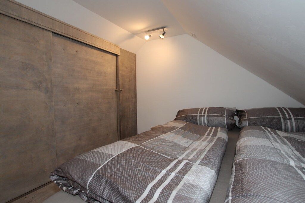 Ein Schlafzimmer mit schrägem Dach, einem Kleiderschrank und einem Bett mit gemusterten Betttextilien.