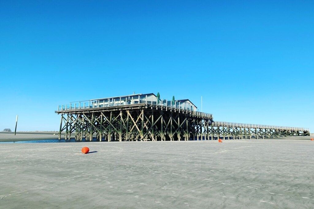 A pier extending into the water with a building on top, surrounded by a clear sky.