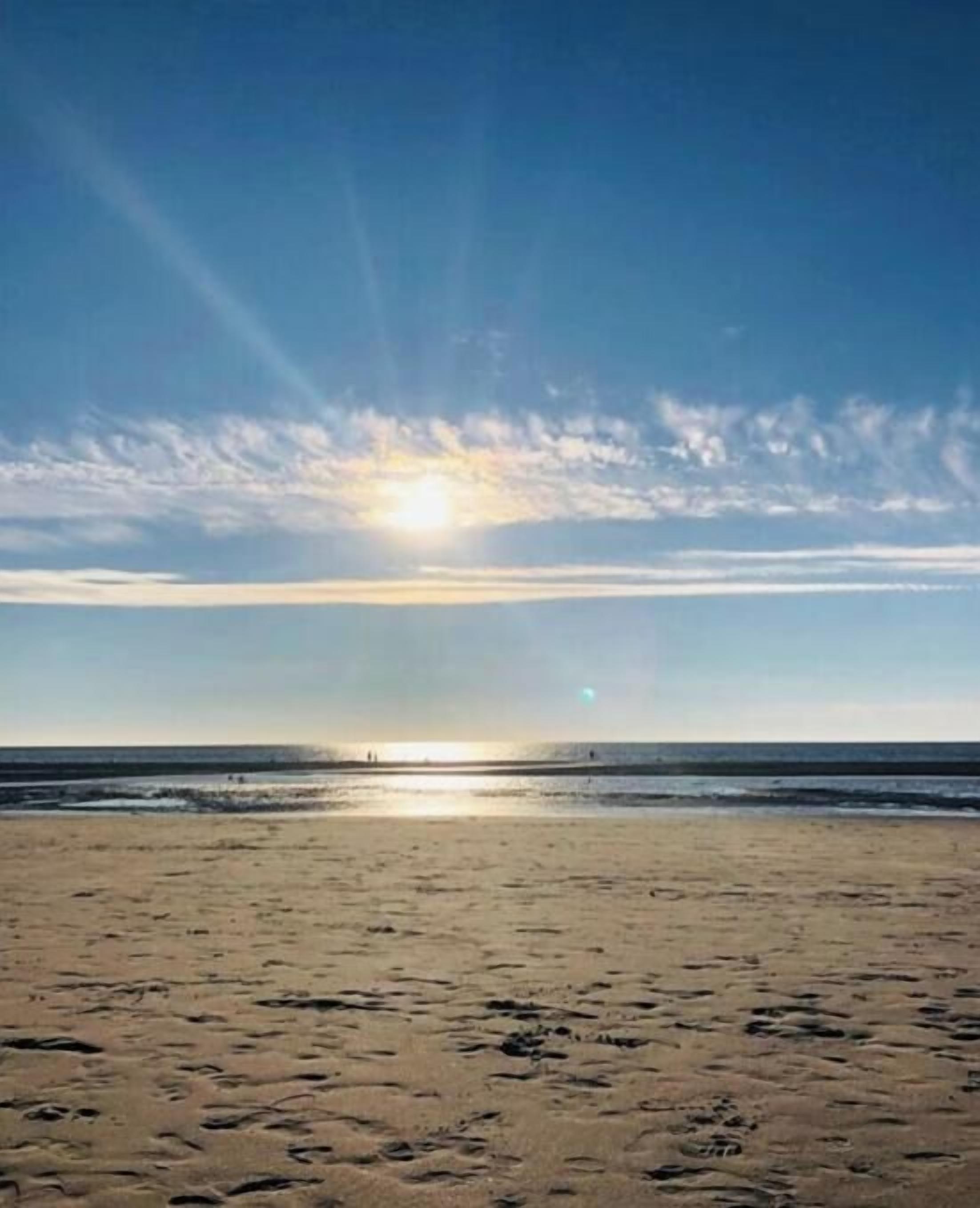Een strand met voetafdrukken in het zand en een heldere lucht.