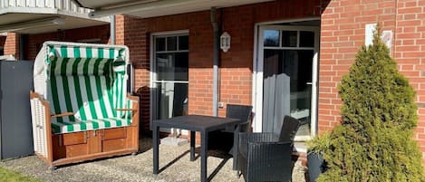 An outdoor seating area with a table and chairs, a covered sofa, and a potted plant.