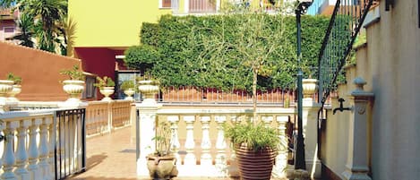 A courtyard with a tiled floor, potted plants, a railing, and a building with balconies.