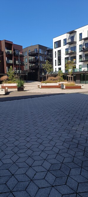 Een modern stadsplein met geometrisch patroon in de bestrating, omgeven door moderne meerlaagsgebouwen met balkons en grote ramen.