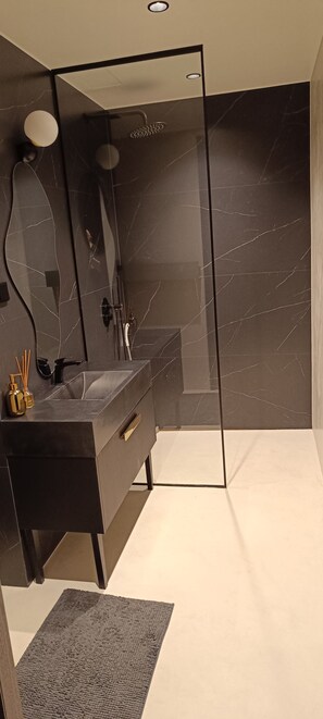 A modern bathroom with a glass-enclosed shower, a vanity with a mirror, and a marble wall. - Kalaranna family & business (Tallinn)