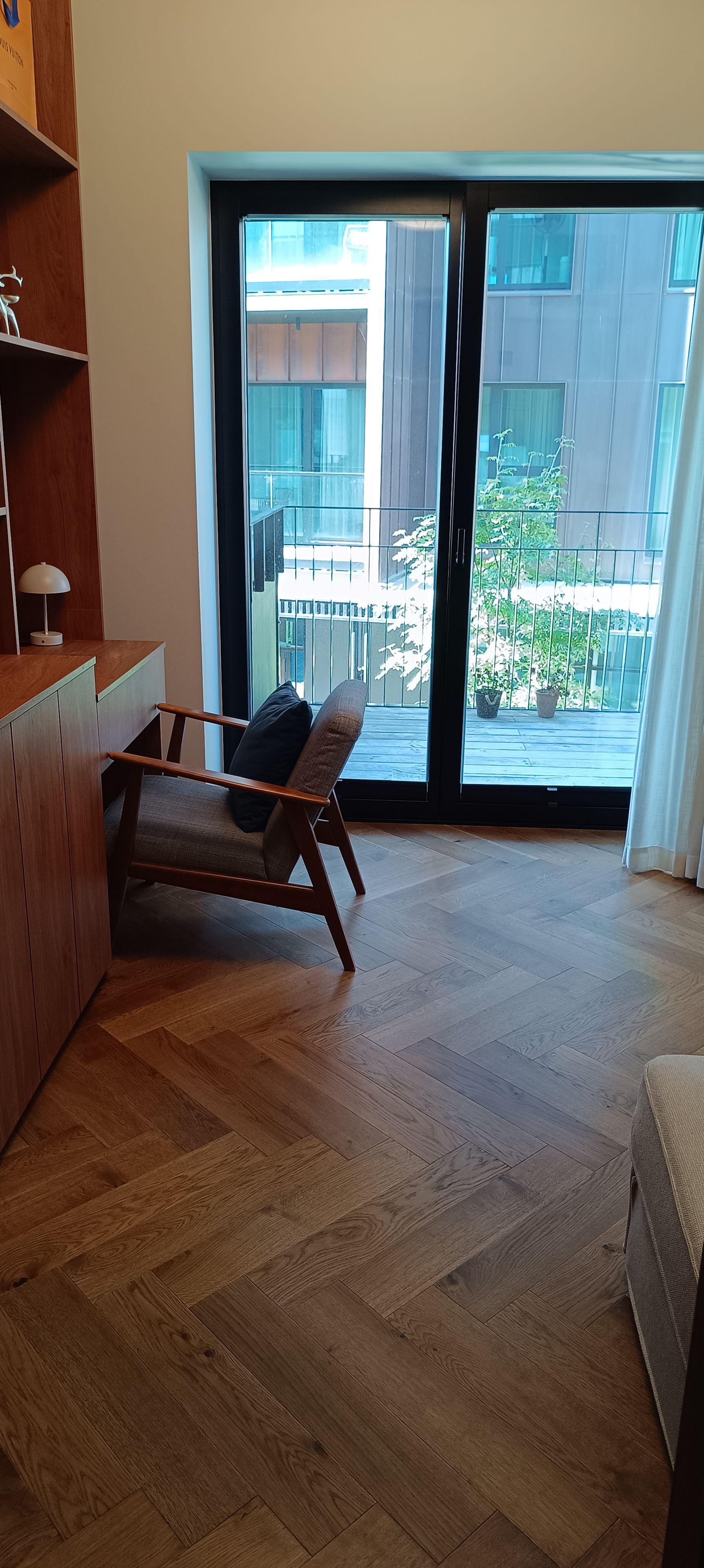 A modern room with a wooden floor, a sofa, a desk, and a large sliding glass door leading to an outdoor balcony.