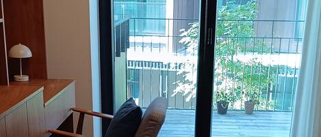 A modern room with a wooden floor, a sofa, a desk, and a large sliding glass door leading to an outdoor balcony.