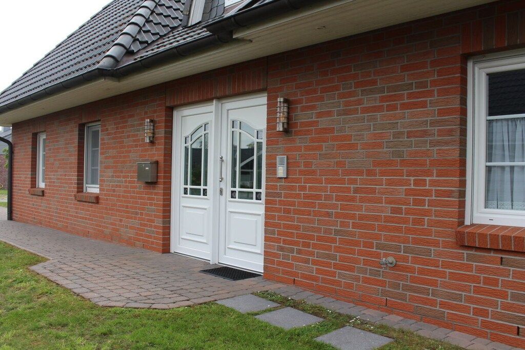 A brick building with a tiled roof, white double doors, and a small window.