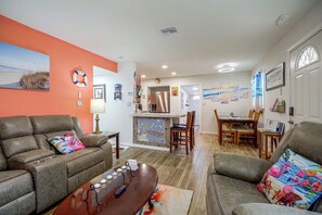 A living room with a sofa, a coffee table, and a dining area with chairs and a table. - 'Trop Rock Inn' Outdoor Oasis & Music Studio (Melbourne)