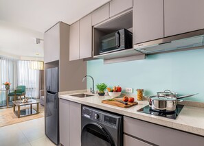 Cocina moderna equipada con lavavajillas, microondas y estufa, zona de comedor con mesa y sillas, y vistas al salón con sofá y ventana.