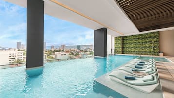 An indoor infinity pool with lounge chairs, a city view, and a green wall.