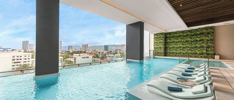 Ein Innenpool im Infinity-Design mit Liegestühlen, Blick auf die Stadt und einer grünen Wand.
