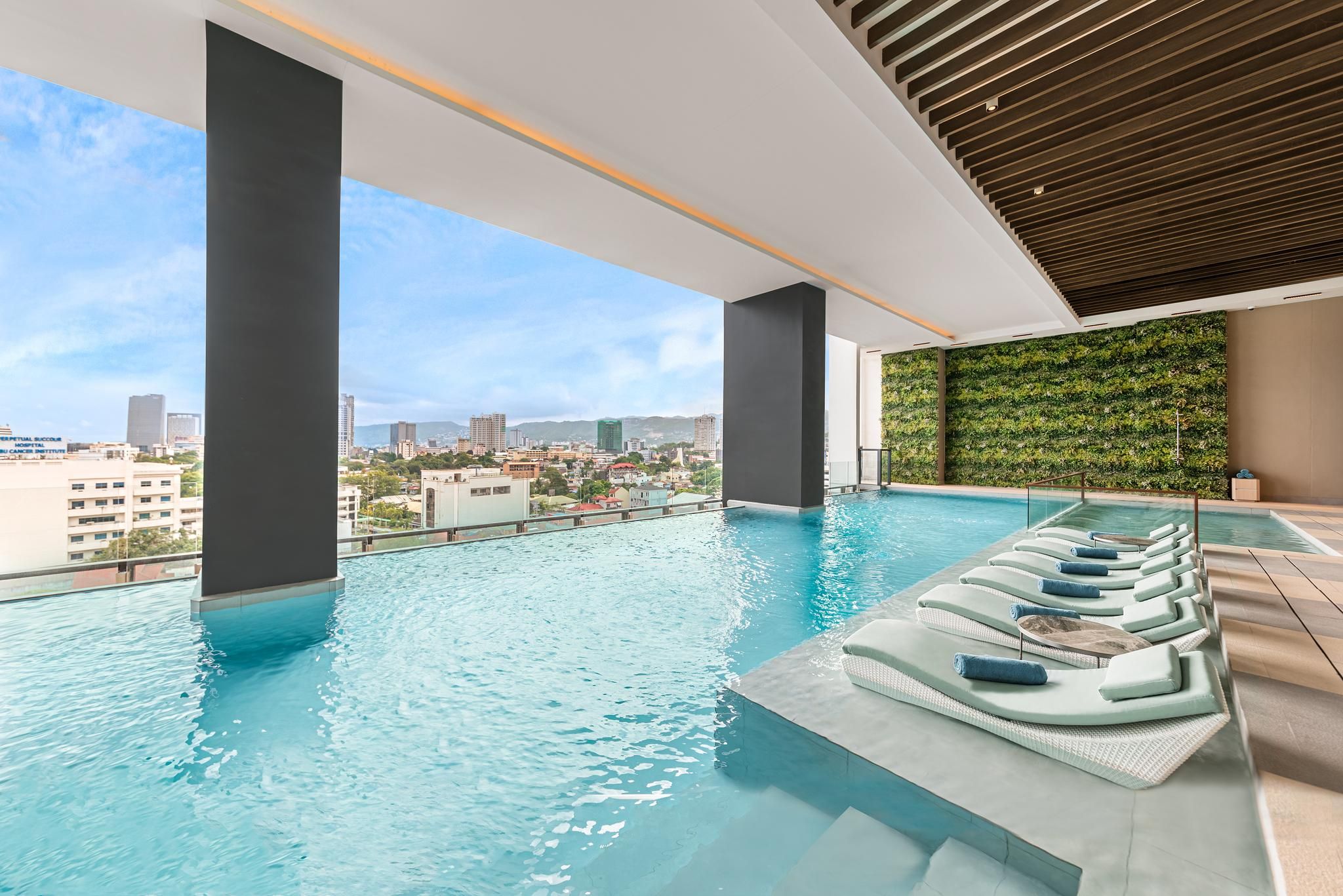 Una piscina de vora infinita a la terrassa amb gandules i vista a la ciutat.