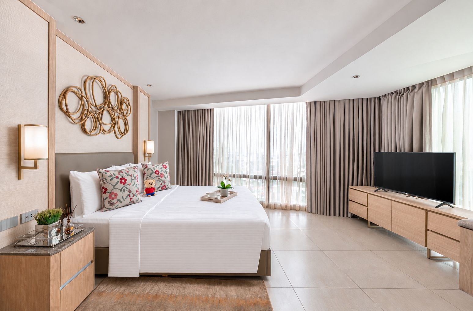 Una habitación de hotel moderna con una cama grande, un televisor de pantalla plana, un mueble de madera y un ventanal con cortinas.