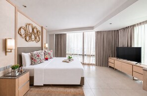 Une chambre d’hôtel moderne dotée d’un grand lit, d’un téléviseur à écran plat, d’une armoire en bois et d’une grande fenêtre avec des rideaux.