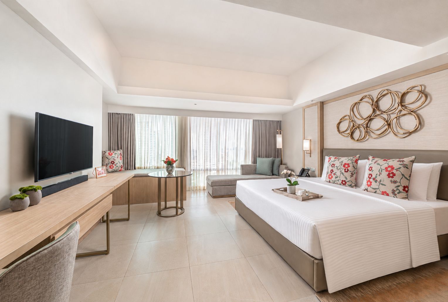 A hotel room with a bed, a desk, a TV, a round table, and a window with curtains.