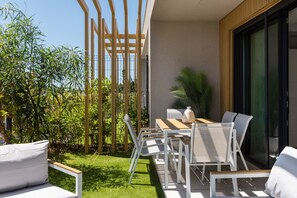 En moderne udendørs terrasse med spisebord, stole og et lille haveområde.