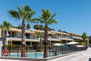 Ein modernes Hotel mit mehreren Balkonen, einem Schwimmbad und Palmen.