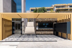 Ein moderner Gebäudeeingang mit einer geometrischen Fassade, einer Treppe und einer Steinwand.