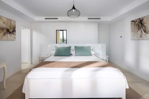 Une chambre à coucher moderne avec un grand lit, deux tables de chevet, un luminaire suspendu et des œuvres d’art accrochées aux murs.