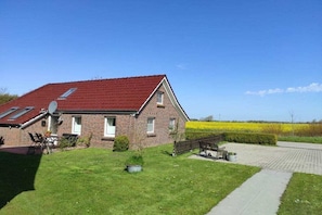 A brick house with a red roof, a paved driveway, and a grassy lawn. - Holiday home in Osteel with swimming pool (Osteel)