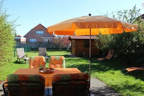 Ein Essbereich im Freien mit Tisch und Stühlen, einem Sonnenschirm und Blick auf ein Haus im Hintergrund.
