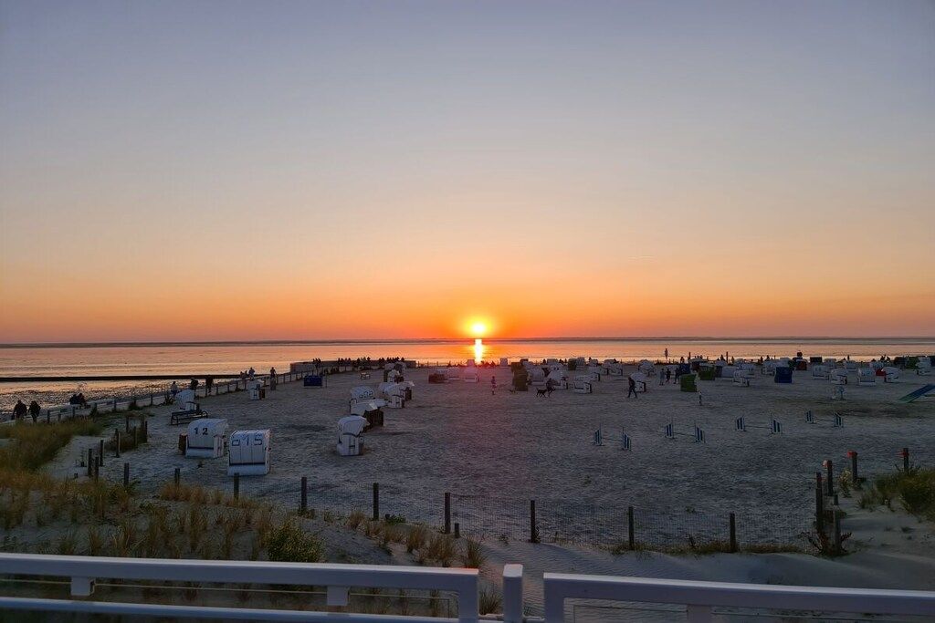 Ein Strand mit Reihen von Strandhütten und einem Sonnenuntergang im Hintergrund.