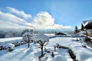 A snow-covered landscape with a building featuring a sloped roof and a visible porch area. - Holiday apartment with 1 bedroom (Reit im Winkl)