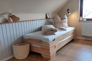 Een kleine, knusse kamer met een schuine kap, een houten bed met opbergladen, een bedlamp en een raam met uitzicht.