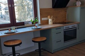 Een keuken met een raam, twee krukken, een spoelbak en een oven.