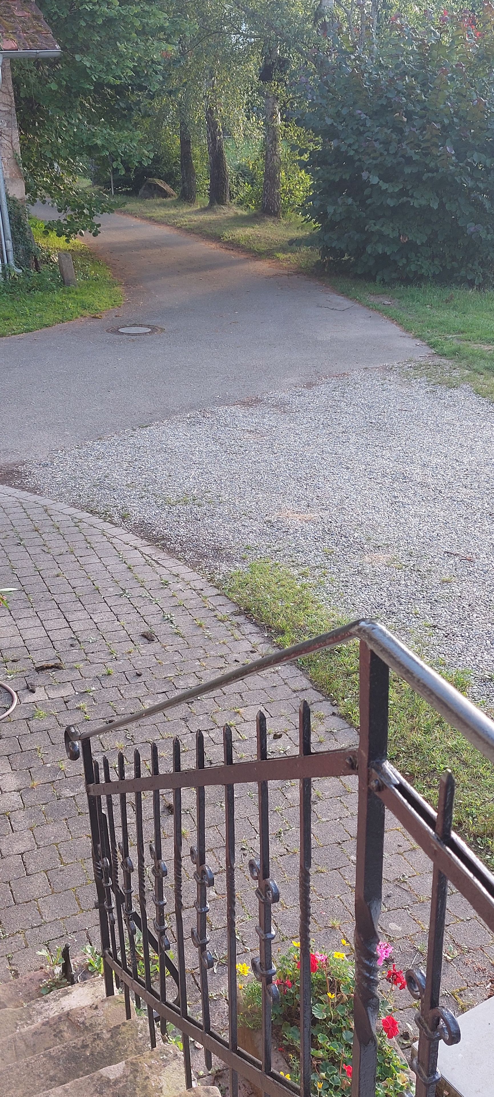 Ein gepflasterter Weg führt zu einem Haus mit einem Metallzaun im Vordergrund.
