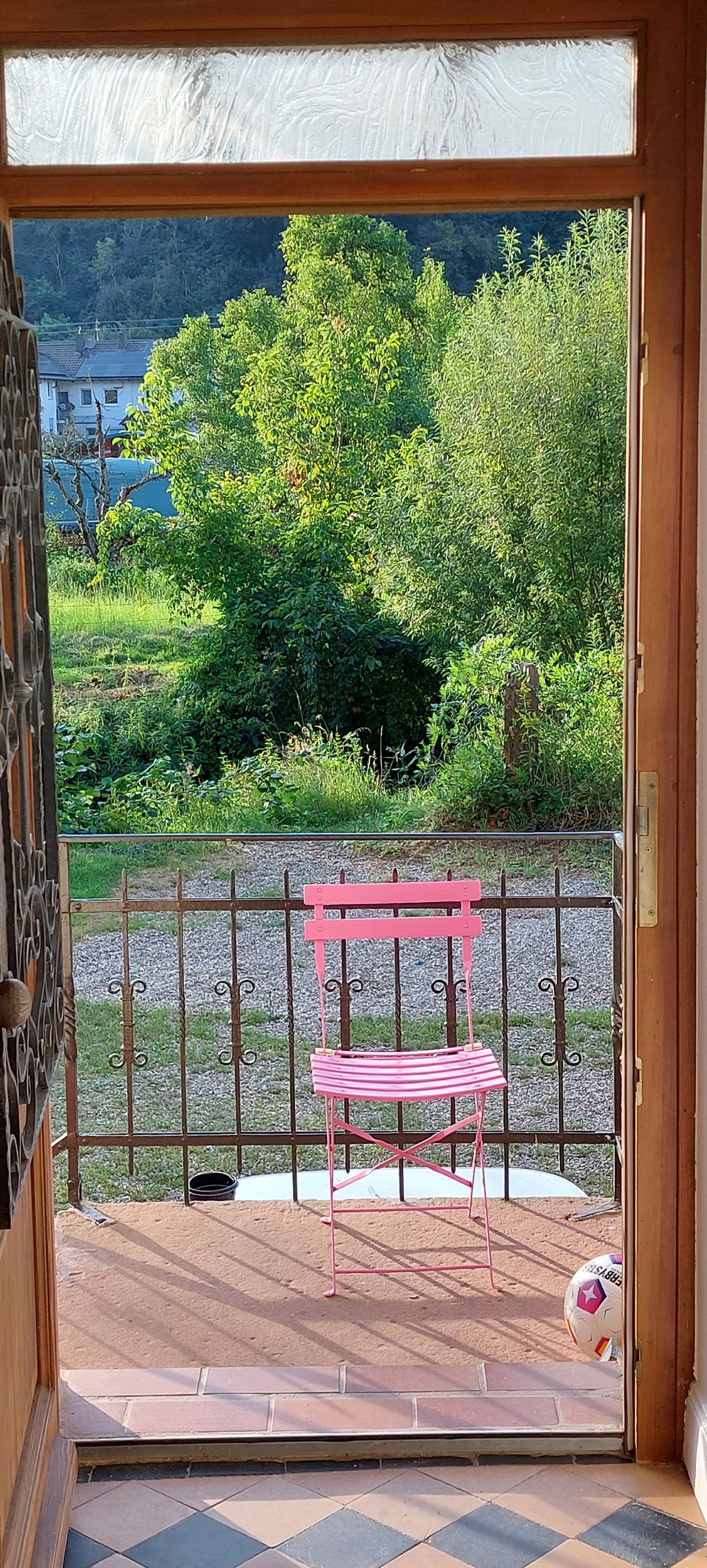 Eine Holzterrasse mit einer rosafarbenen Bank, einem Metallzaun und Blick auf eine grüne Landschaft.