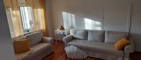 A living room with a sofa, a small table, and a window with curtains.