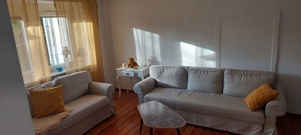A living room with a sofa, a small table, and a window with curtains.