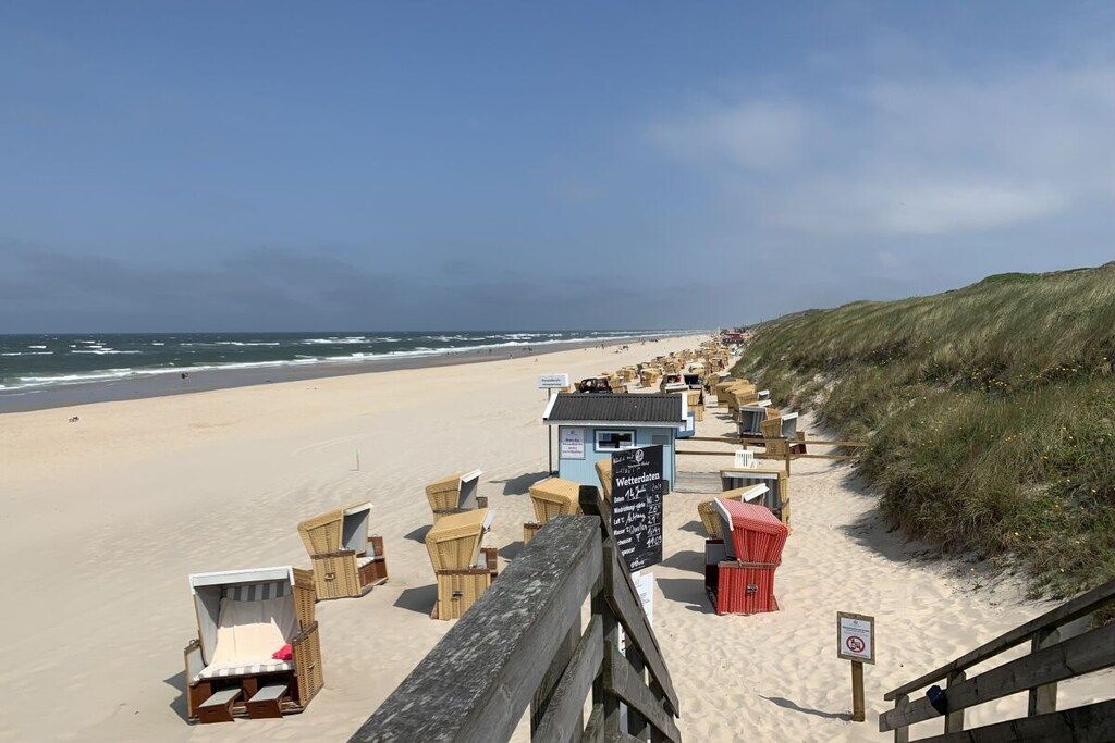 Eine Lage am Strand mit einer Holzstege, der zu Liegestühlen und einem kleinen Gebäude, vermutlich einer Strandhütte oder einem Imbissstand, führt.