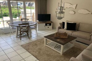 Ein Wohnzimmer mit Fernseher, einer Couch, einem Couchtisch und einem Essbereich mit Stühlen.