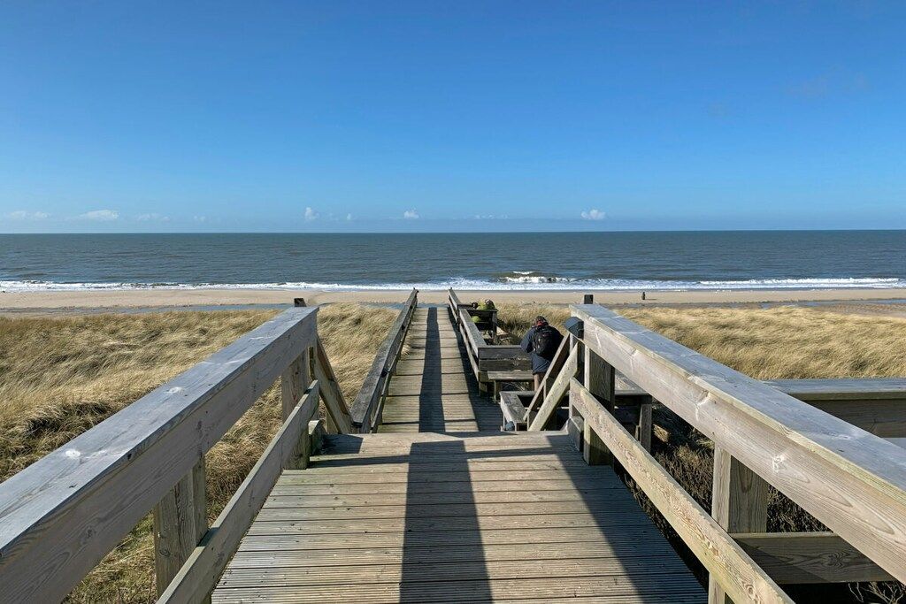 En träpromenad som leder till en strand med fri utsikt över havet.