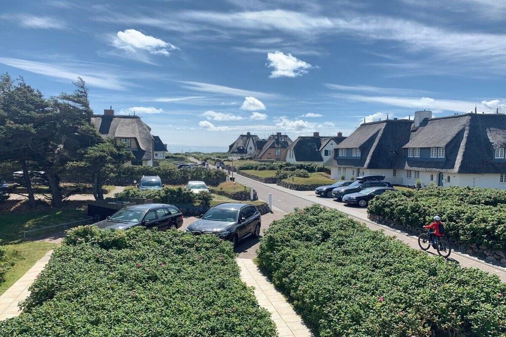 A residential street with houses, parked cars, and a cyclist.