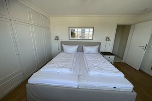Uma cama de casal com duas almofadas, uma mesinha de cabeceira e um criado-mudo.