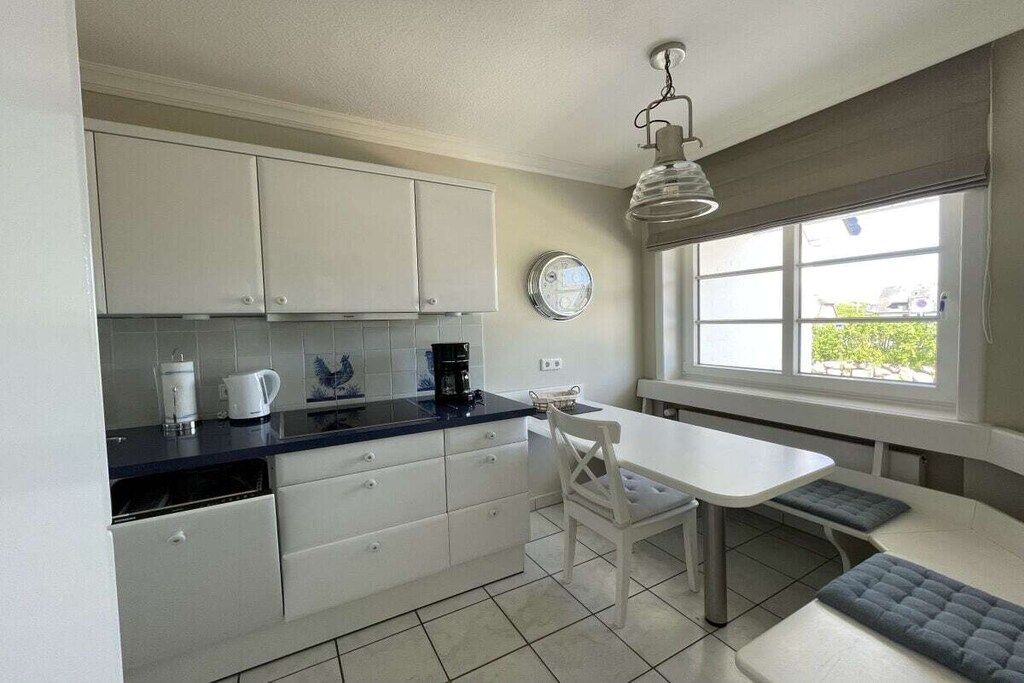 A kitchen with white cabinets, a black countertop, a white dining table with benches, and a window with a view.