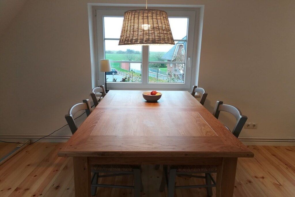 A dining area with a wooden table and chairs, a hanging lamp, and a window with a view of the outside.