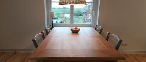 A dining area with a wooden table and chairs, a hanging lamp, and a window with a view of the outside.