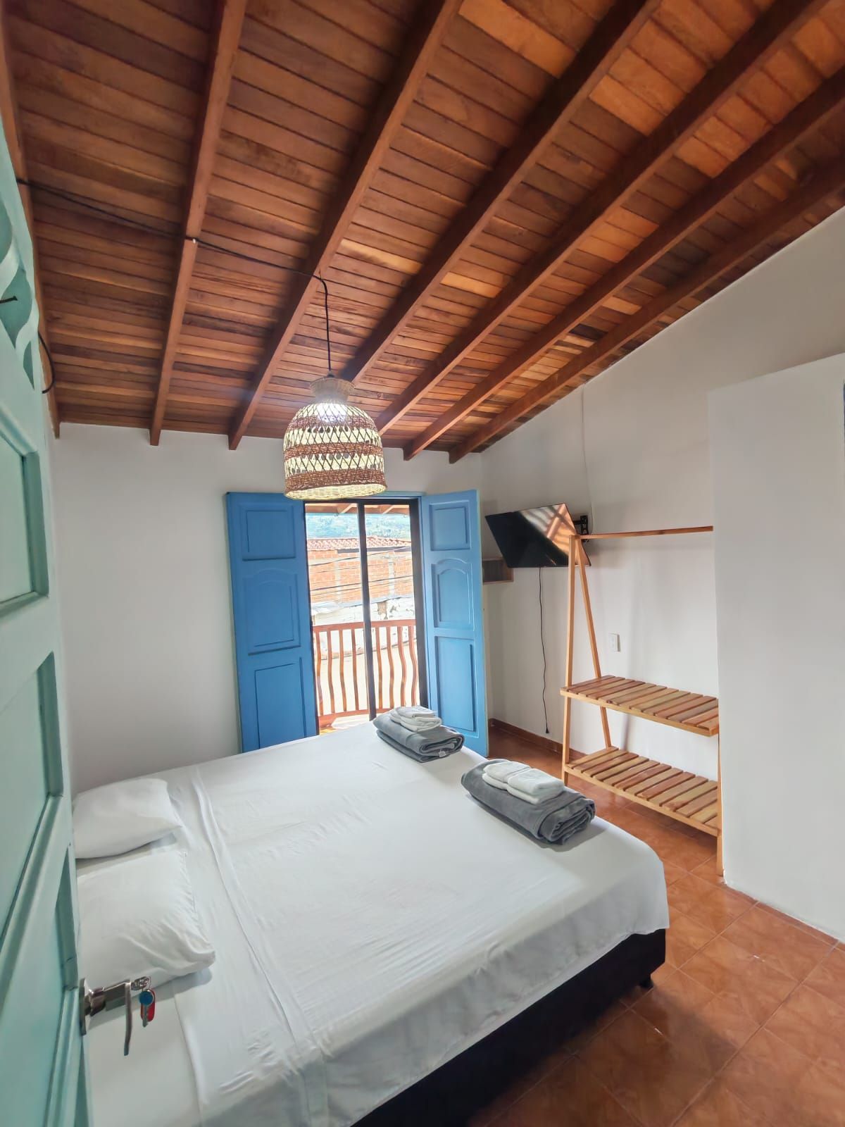 A bedroom with a wooden ceiling, a bed with white linens, a hanging light fixture, and a blue door.