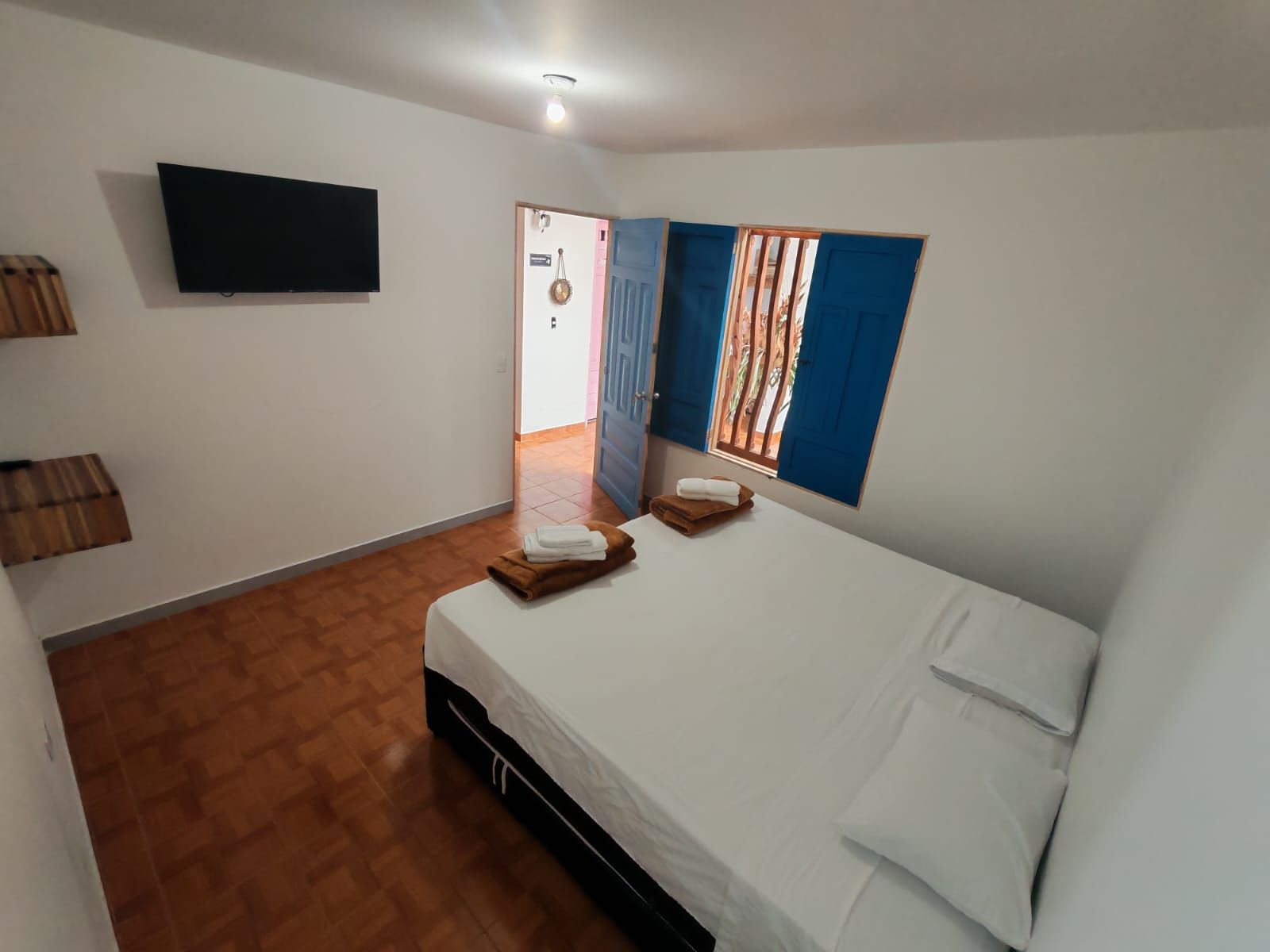 A hotel room with a bed, a flat-screen TV mounted on the wall, and a window with blue curtains.