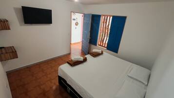 A hotel room with a bed, a flat-screen TV mounted on the wall, and a window with blue curtains.
