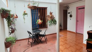Un espacio interior amplio con piso de madera, una mesa de comedor con sillas, macetas colgantes y una puerta rosa.