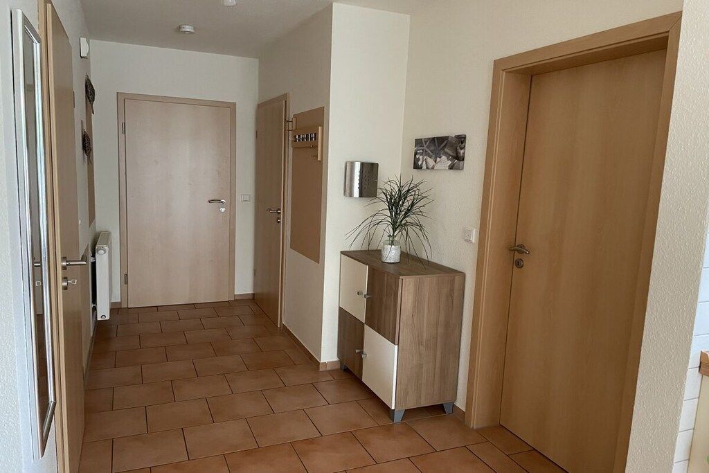 A hallway with a wooden door, a cabinet with a plant, and a wall-mounted light fixture.