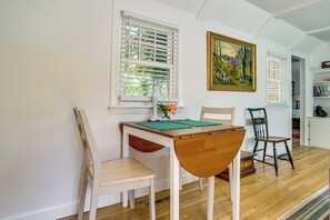 Een eethoek met een houten tafel, twee stoelen, een vaas met bloemen en een schilderij aan de muur.