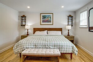 A bedroom with a large bed, two bedside tables with lamps, a bench, a framed painting on the wall, and a window with blinds. - 3 Mi to Craigville Beach! Walkable Couple’s Haven (Osterville)