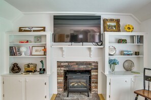 A living room with a fireplace, television, and shelves with books and decorative items. - 3 Mi to Craigville Beach! Walkable Couple’s Haven (Osterville)